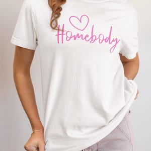 May include: White t-shirt with a pink heart and the text "Homebody" in pink script.
