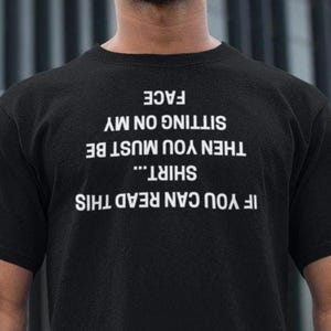 May include: Black t-shirt with white text that reads "If you can read this shirt... then you must be sitting on my face."