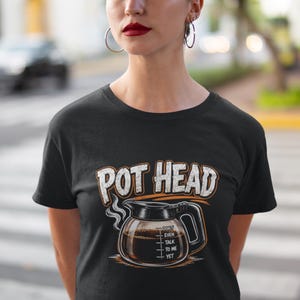 Może przedstawiać: Czarny t-shirt z grafiką szklanego dzbanka do kawy, z którego unosi się para. Napis "POT HEAD" jest wydrukowany dużymi białymi literami nad dzbankiem, a słowa "DON'T EVEN TALK TO ME YET" znajdują się na samym dzbanku do kawy.