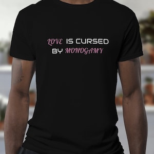 May include: Black t-shirt with the text "LOVE IS CURSED BY MONOGAMY" in a pink and white script. The shirt is a crew neck style and appears to be made of a soft material. The text is centered on the chest.