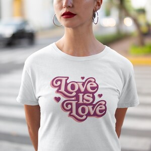 May include: White t-shirt with a pink and white graphic that says "Love is Love" in a retro font.