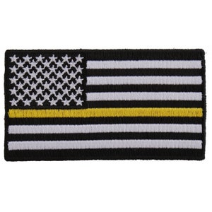 May include: Embroidered patch featuring a stylized American flag design. The flag has a black background with white and black stripes, white stars, and a yellow stripe. The patch is rectangular and likely intended for application on clothing or gear.