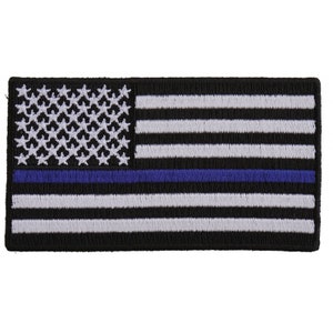 May include: Embroidered patch depicting a stylized American flag. The design features a black background with white stripes and stars, and a blue line. The rectangular patch is designed for attachment to garments or accessories.