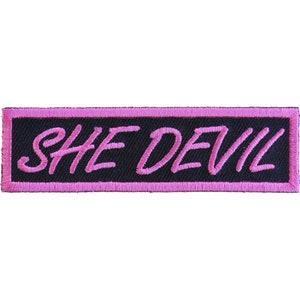 May include: Pink embroidered patch with the text "SHE DEVIL" on a black background.