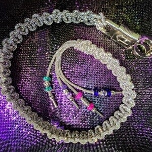 May include: A silver chain whip with a silver clasp and a beaded tassel. The tassel has turquoise, purple, and pink beads.