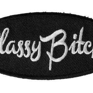 May include: White embroidered patch on a black oval background with the text "Classy Bitch".