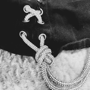 May include: A black garment with white lace-up detailing and a silver chain with rhinestones hanging from the bottom.