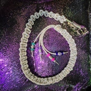 May include: A white braided whip with silver accents and colorful beads. The whip has a silver handle and a loop at the end.