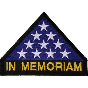 May include: A blue and white triangular patch with a black border and the words "IN MEMORIAM" in yellow letters. The patch features a stylized American flag with white stars on a blue background.