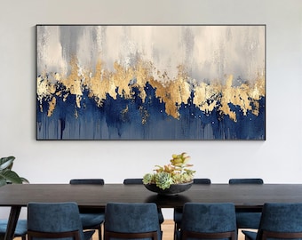 Op de afbeelding: Abstract schilderij met blauwe en gouden accenten. Het schilderij hangt boven een eettafel met blauwe stoelen.