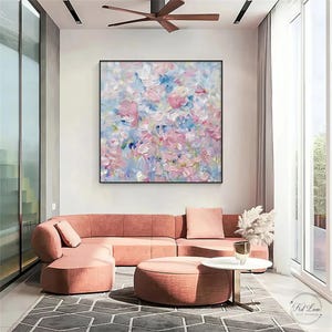 May include: A square abstract oil painting featuring thick, textured impasto brushstrokes in shades of soft pink, light blue, white, and lavender. The artwork is displayed in a thin black frame, showcasing a layered, expressive composition of colours.