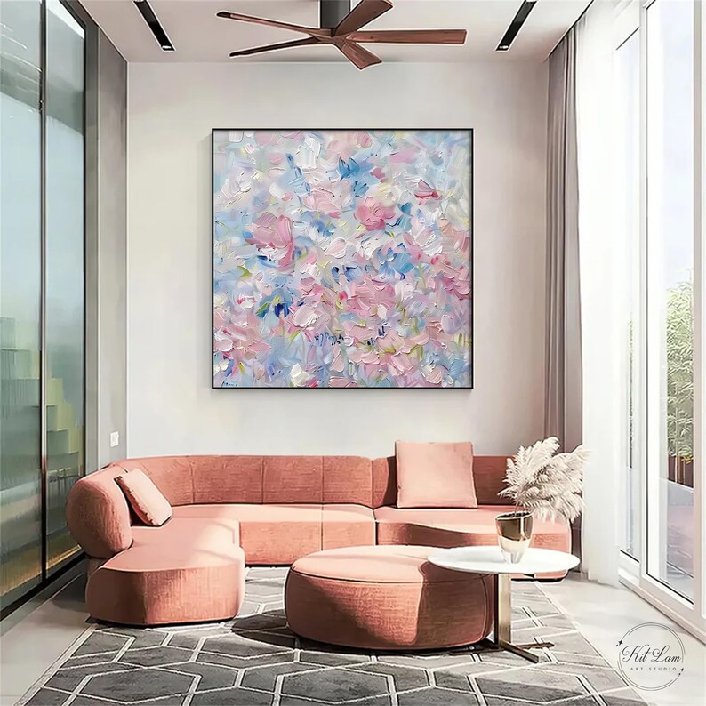 May include: A square abstract oil painting featuring thick, textured impasto brushstrokes in shades of soft pink, light blue, white, and lavender. The artwork is displayed in a thin black frame, showcasing a layered, expressive composition of colours.
