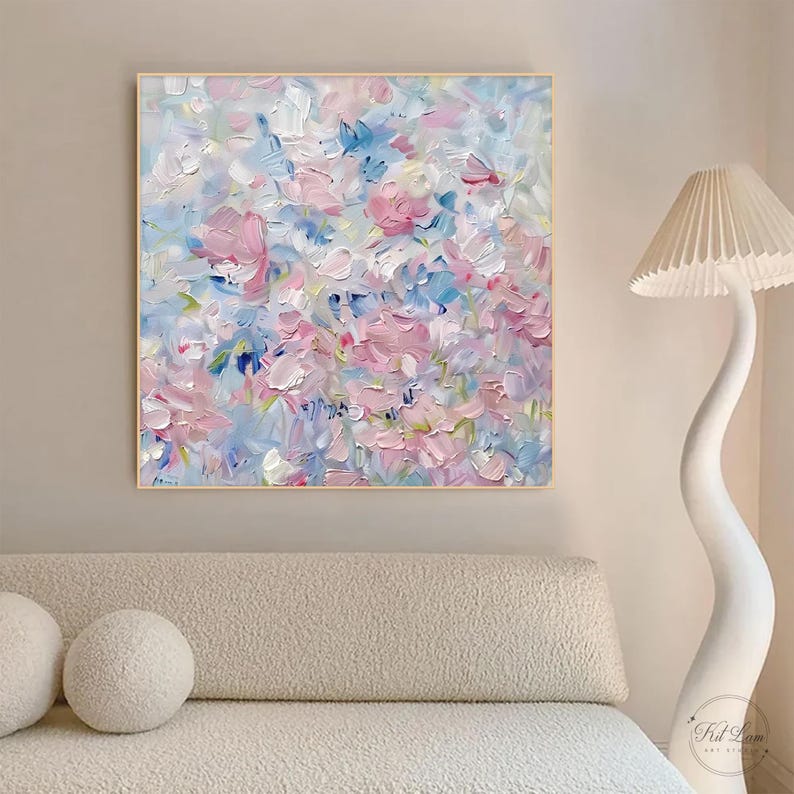 May include: A square oil painting on canvas featuring thick, textured impasto brushstrokes in shades of soft pink, white, and light blue. The abstract composition creates a floral-like pattern with layered paint, framed in a thin light wood border.