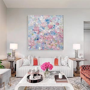 May include: A square canvas painting featuring thick, textured impasto brushstrokes in shades of soft pink, sky blue, and white. The abstract composition displays layered dabs of paint that create a sense of depth and movement across the surface.