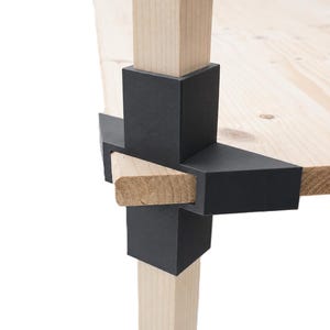 Peut inclure: Gros plan sur une table en bois avec un plateau et des pieds de couleur claire. La table est dotée de supports métalliques noirs qui relient les pieds au plateau. Le grain du bois est visible sur le plateau et les supports en bois.