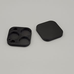 Op de afbeelding: Zwart 3D-geprint accessoire met een vierkante vorm en afgeronde hoeken. Het heeft vier cirkelvormige inkepingen van verschillende grootte en een apart vierkant stuk. De items liggen op een lichtgrijze ondergrond.