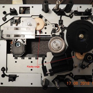Puede incluir: Primer plano de un mecanismo de reproductor de CD con un engranaje negro y un piñón plateado. El texto "17.08.2018 19:43" es visible en la esquina inferior derecha. La imagen muestra un piñón defectuoso con el texto "Faulty cogs" escrito al lado.