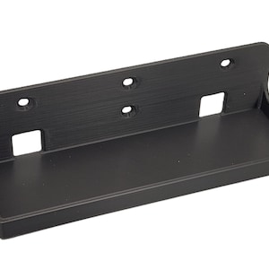 Puede incluir: Una estantería de pared negra y rectangular con una superficie texturizada. Cuenta con una pequeña bandeja empotrada y varios orificios circulares para el montaje. La estantería mide aproximadamente 20 cm de ancho y 10 cm de profundidad.