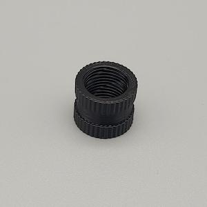 May include: Two black cylindrical connectors stacked. Each has a ridged exterior and a threaded interior. The connectors are made of a matte black material, set against a plain, light grey background. The connectors are likely used for plumbing.