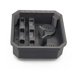 May include: A black, 3D-printed storage container with multiple compartments. The container has sections labeled with numbers and measurements, including "1/2" 13mm". The design is geometric and functional, suitable for organizing small items.