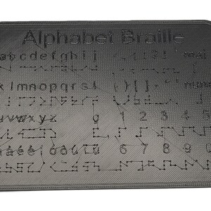 May include: A dark grey rectangular Braille alphabet chart. The text "Alphabet Braille" is at the top, followed by the alphabet, numbers, and punctuation in raised dots. The surface has a textured pattern.