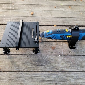 Può includere: Un utensile rotante nero e blu con una staffa di montaggio nera e un accessorio per sega da tavolo nero. L'utensile ha la scritta "WORX 20V" stampata. L'accessorio per sega da tavolo ha una base nera con una superficie scanalata.