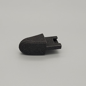 Peut inclure: Un petit composant en plastique noir avec une surface texturée. La pièce a une extrémité arrondie et une section rectangulaire avec une fente. L'objet fait probablement partie d'un mécanisme ou d'un appareil plus grand.