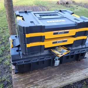 May include: A black and yellow DeWalt T-STAK tool box system with two stacked boxes and a larger black box underneath. The boxes have a yellow trim and the text "T-STAK" printed on them.
