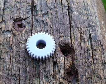 May include: A white plastic gear with a hole in the centre, sitting on a weathered wooden surface.