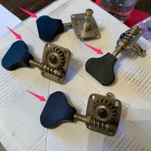 May include: Four vintage black and gold guitar tuning keys with a square base and a round gear. The keys have a black plastic knob.