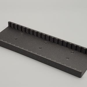 May include: A black plastic storage tray with a textured surface and multiple holes. The tray has a raised edge around the perimeter.
