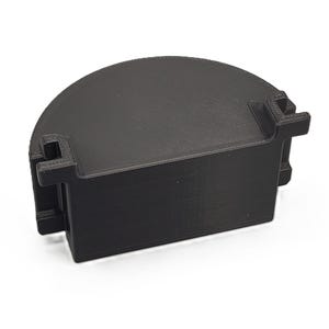 Może przedstawiać: Czarny, półkolisty obiekt drukowany w 3D z prostokątną podstawą i dwoma wystającymi zakładkami. Górna powierzchnia jest zakrzywiona. Obiekt wykonany jest z matowego, czarnego materiału.