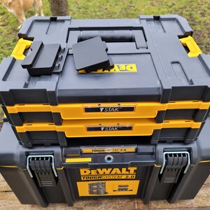 May include: A stack of three black and yellow DeWalt ToughSystem 2.0 tool boxes. The top box has a black T-STAK label. The middle box has a black T-STAK label. The bottom box has a black DeWalt ToughSystem 2.0 label.