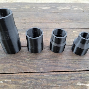 May include: Four black plastic tubes of varying sizes. The tubes are cylindrical and have a smooth, slightly textured surface.