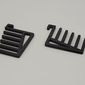 Könnte beinhalten: Zwei schwarze, geometrische 3D-gedruckte Objekte. Jedes hat eine rechteckige Basis mit vertikalen Stäben. Eines hat eine hakenartige Verlängerung. Die Objekte befinden sich auf einer hellgrauen Oberfläche.