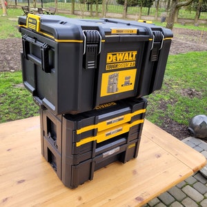以下が含まれることがあります： 黒と黄色の DeWalt ToughSystem 2.0 ツールボックスが、黒と黄色の DeWalt 3 段引き出しツールボックスの上に積み重ねられています。