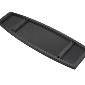 Könnte beinhalten: Eine schwarze rechteckige Ablage mit erhöhten Kanten und zwei vertieften Abschnitten. Die Ablage hat eine strukturierte Oberfläche und vier kleine Löcher. Die Gesamtform ist länglich, mit abgerundeten Enden.