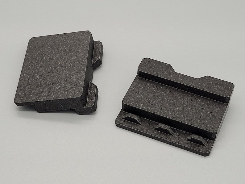 May include: Two black plastic 3D printed pieces with interlocking edges. The pieces are designed to connect together to create a larger structure.