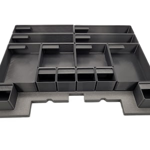 Könnte beinhalten: Ein dunkelgrauer Organizer mit mehreren Fächern unterschiedlicher Größe. Der Organizer hat mehrere rechteckige und quadratische Abschnitte, die für die Aufbewahrung und Organisation bestimmt sind. Die Fächer sind in einem strukturierten Layout angeordnet.