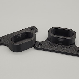 Może przedstawiać: Dwa czarne wsporniki drukowane w 3D z owalnym otworem i dekoracyjnym wzorem kwiatowym. Każdy wspornik ma dwa otwory do montażu. Wsporniki są przeznaczone do trzymania przedmiotu.