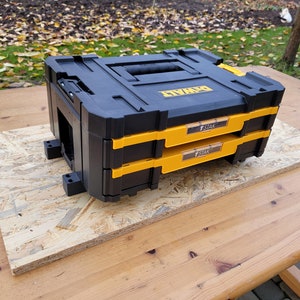 Może przedstawiać: Dwa czarne i żółte, składane skrzynki na narzędzia z nadrukiem "DEWALT" i "T-STAK" na boku.