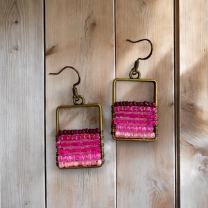 May include: A pair of pink and purple beaded earrings with a square frame and a gold finish.