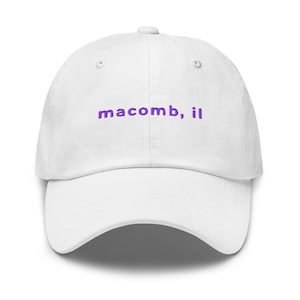 May include: White baseball cap with the embroidered text "macomb, il" in purple. The cap has a curved brim and a structured crown. A casual accessory for everyday wear.