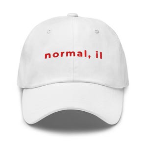 May include: White baseball cap with the red text "normal, il" embroidered on the front. The cap has a curved brim and a button on top. The hat is made of a soft material.