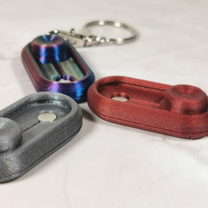 Puede incluir: Tres llaveros con una función de trompo. Uno es plateado, otro rojo y otro es de color arcoíris iridiscente.