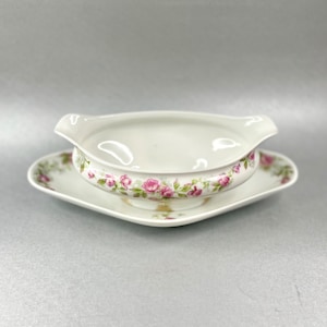 Könnte beinhalten: Weiße Porzellansauce mit einem Blumendesign aus rosa Rosen und grünen Blättern. Die Sauce steht auf einem passenden quadratischen Teller.