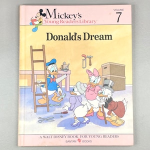 May include: A vintage children's book titled "Donald's Dream" from the Mickey's Young Readers Library series. The cover features illustrations of Donald Duck, Daisy Duck, Scrooge McDuck, and other characters in a workshop setting. Published by Bantam Books.