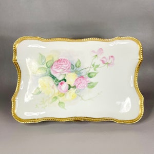 Puede incluir: Una bandeja de servir de porcelana blanca con un borde dorado y un diseño floral pintado a mano con rosas rosas y amarillas.