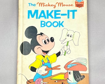 Op de afbeelding: Een vintage kinderboek met Mickey Mouse met de titel "The Mickey Mouse Make-It Book". Mickey houdt een papieren olifant vast en gebruikt een schaar en plakband om knutselwerkjes te maken.