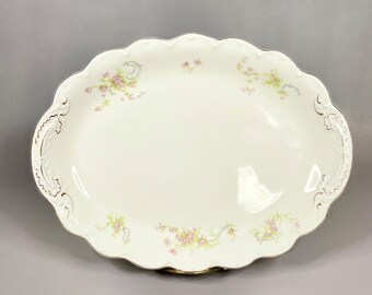 May include: White oval serving platter with a scalloped edge and delicate floral pattern in pink and green. The platter has two ornate handles on either side.